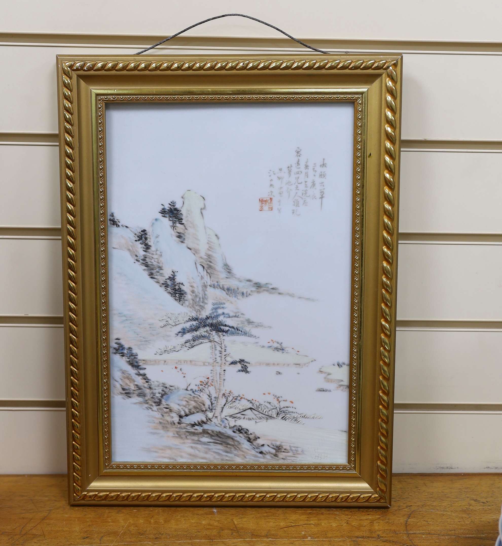 A Chinese enamelled porcelain plaque, decorated with a mountainous landscape and calligraphy, framed, overall 47cm x 34cm